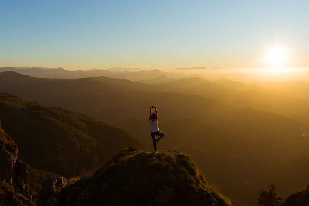 Person practicing yoga atop a mountain at sunrise, embodying personal growth